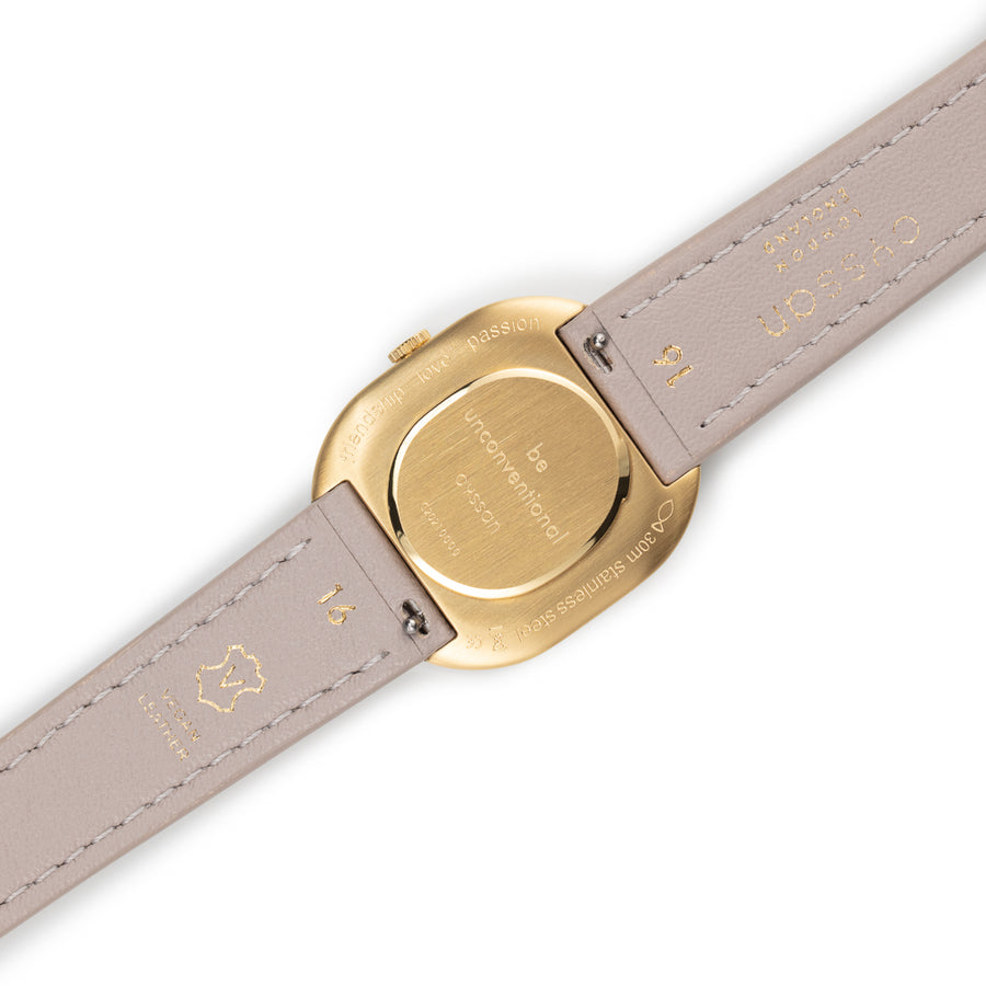 View of the gold caseback showing the engraved words, friendship, love, passion, be unconventional, and the sand-coloured, vegan-leather strap.