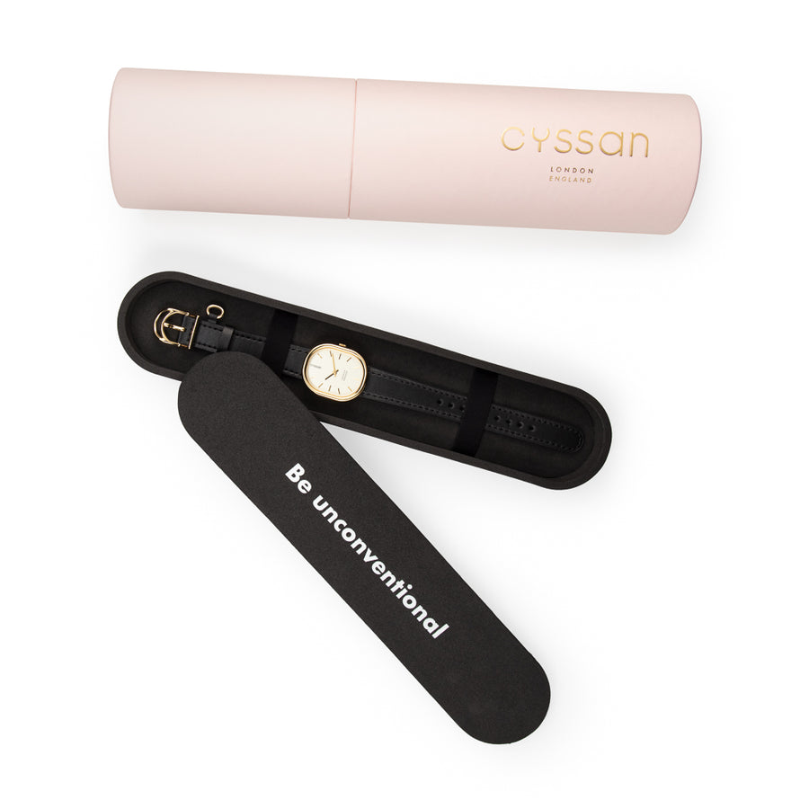 the Cyssan pink cylindric packaging. The black-foam inner packaging is open and there is a watch with a gold-plated watch case and black watch strap placed inside. It is held in place with two black elastic straps.