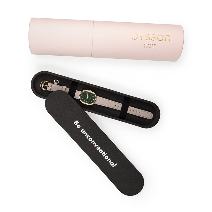 Pink cylindric outer packaging, black inner packaging holding a woman's watch with a green dial, gold-tone case and sand-coloured strap
