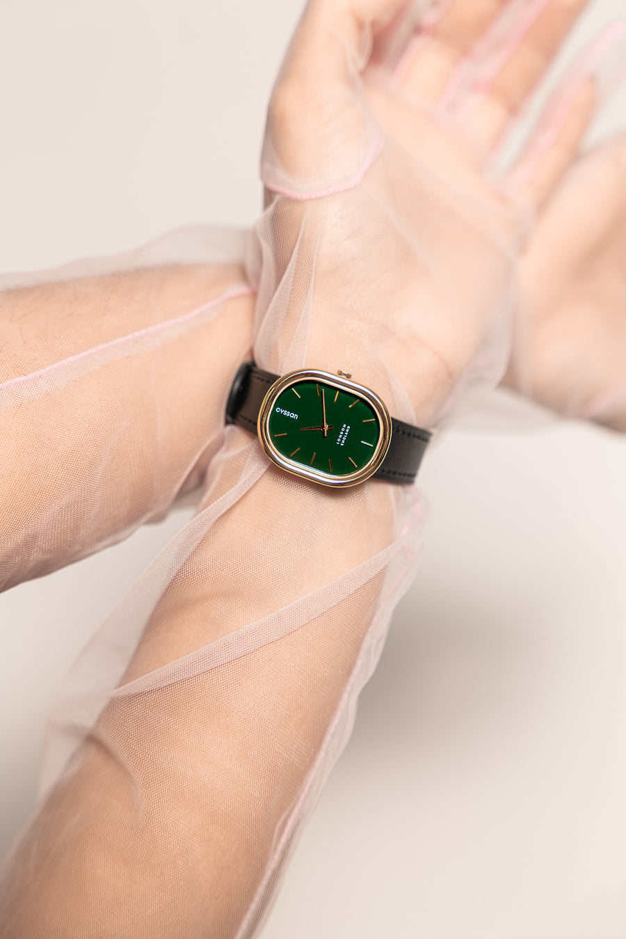A close-up of a woman's arms and hands, She's wearing long, sheer-pink tulle gloves and a watch with a gold case, green dial and black strap