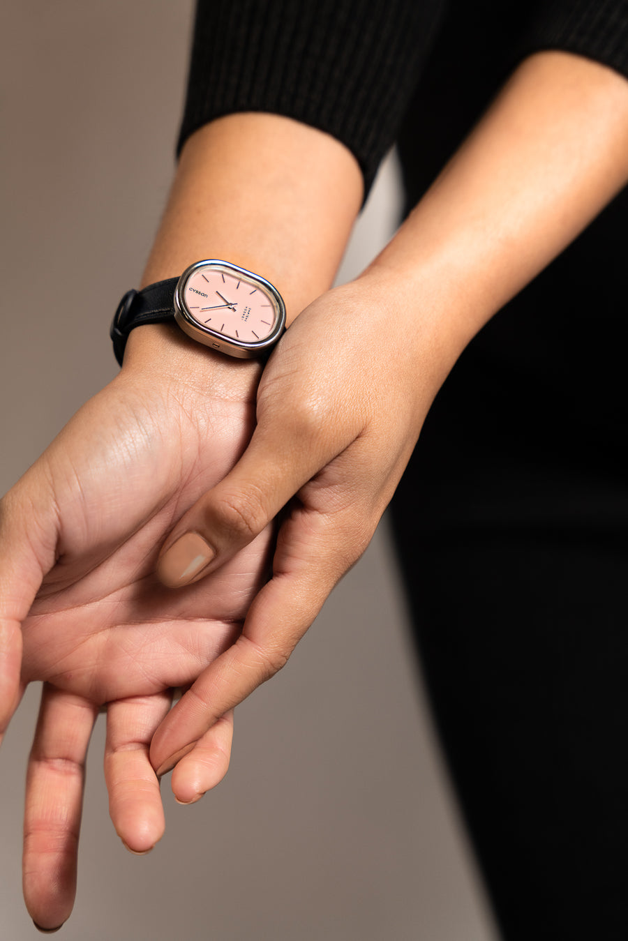 A close-up of a woman's hands and wrists. She's wearing a watch with silver case, pink dial and blue strap