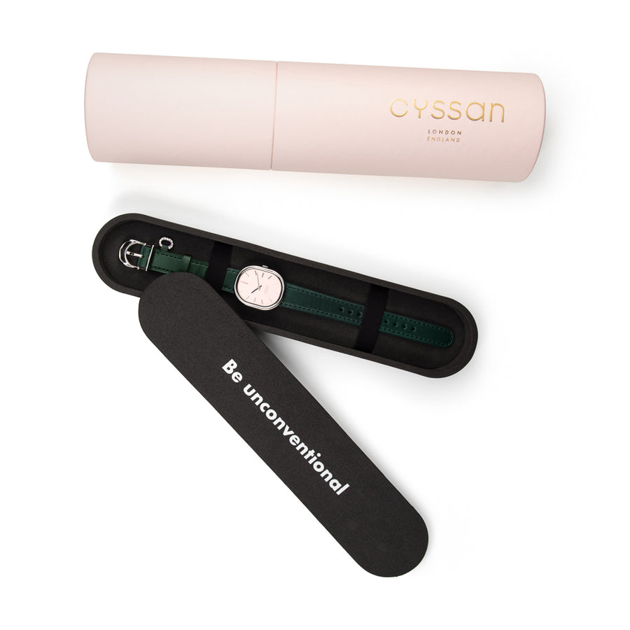 Pink cylindric outer packaging, black inner packaging holding a woman's watch with a pink dial, silver-tone case and green strap