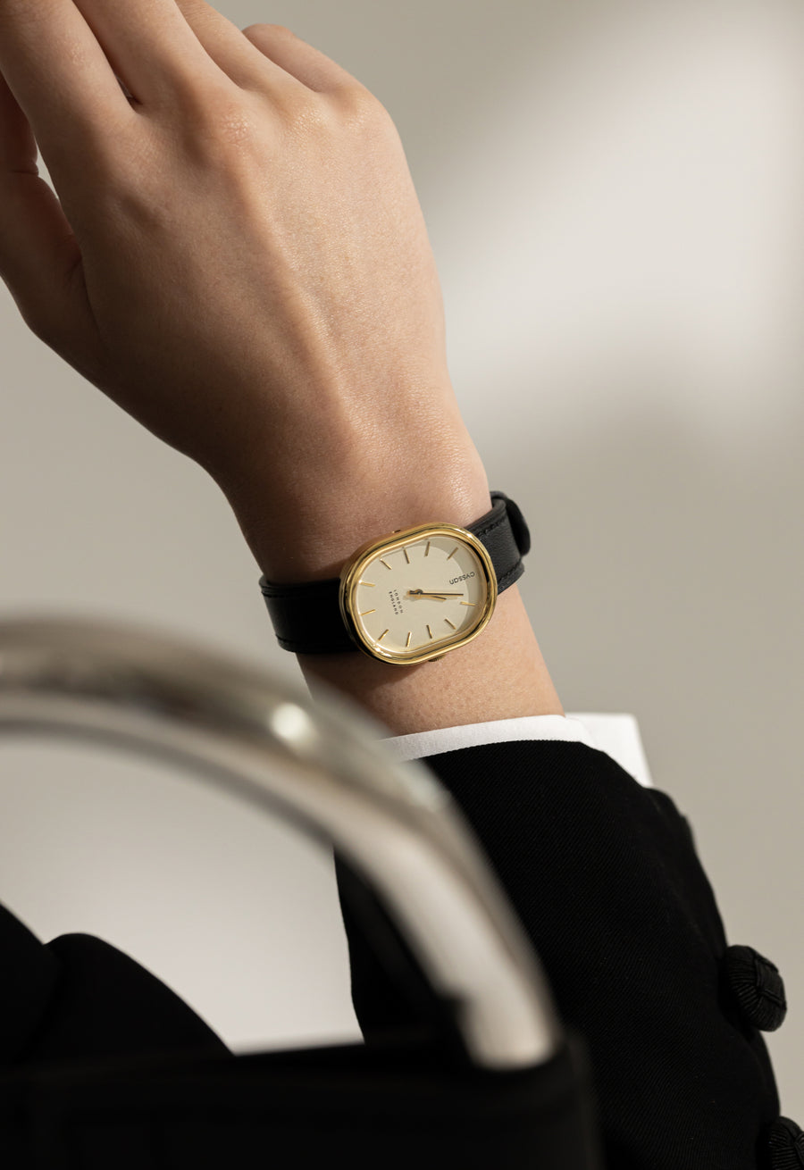 model wearing cyssan watch with gold case, champagne dial, gold index and hands, and black vegan-leather strap