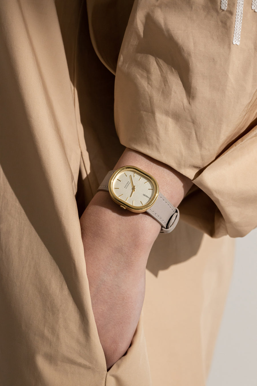 a close-up of a model's arm with her hand in her pocket. on her wrist is a Cyssan watch with a gold watch case, and sand-coloured strap..