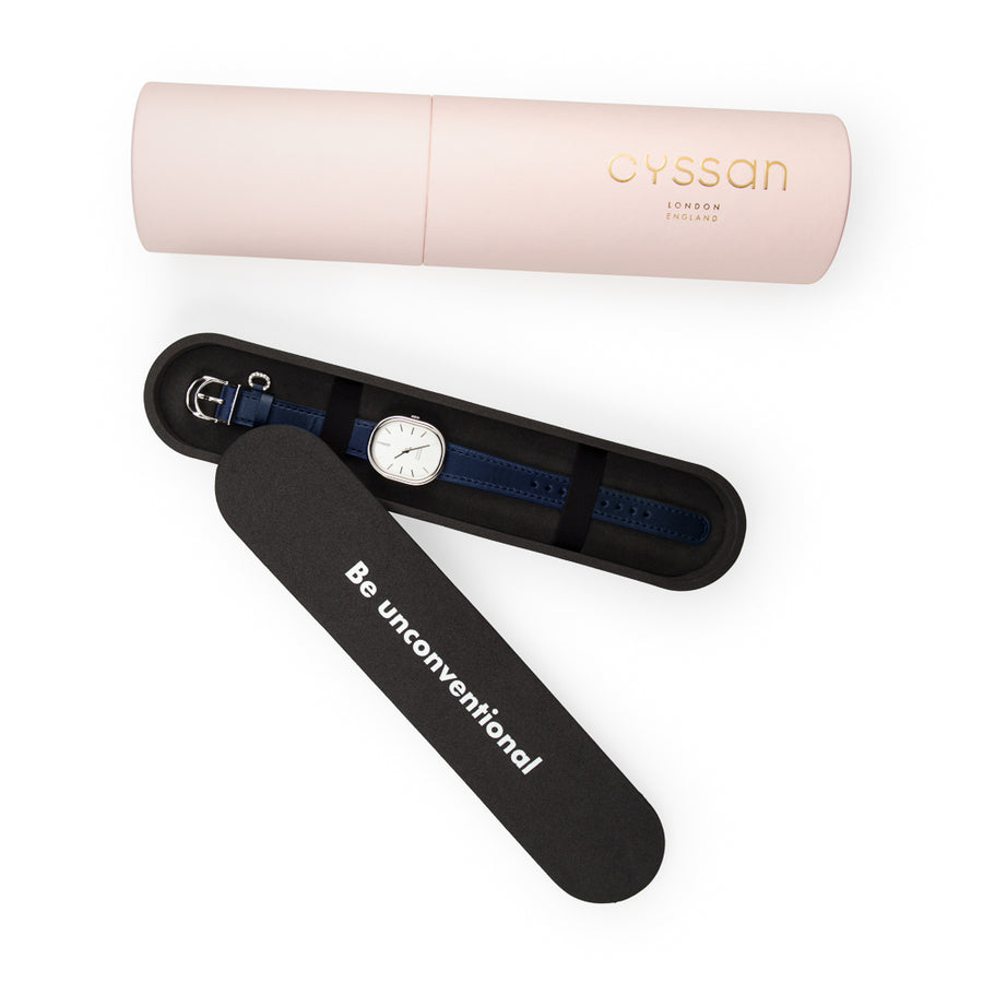 the Cyssan pink cylindric packaging. The black-foam inner packaging is open and there is a watch with a stainless steel watch case and dark blue watch strap placed inside. It is held in place with two black elastic straps.